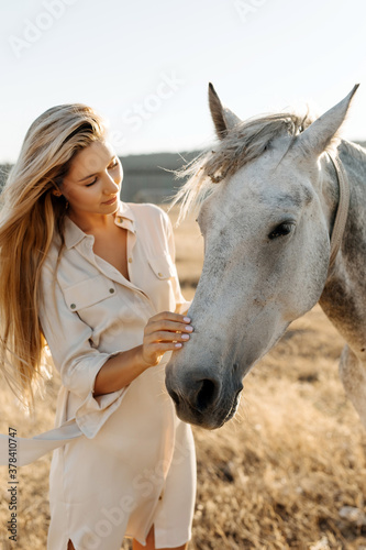 Young blonde woman petting a horse in a field.