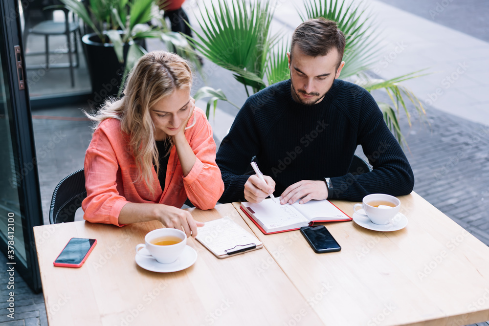 Fototapeta premium Attentive colleagues with clipboard and notebook working outside cafe
