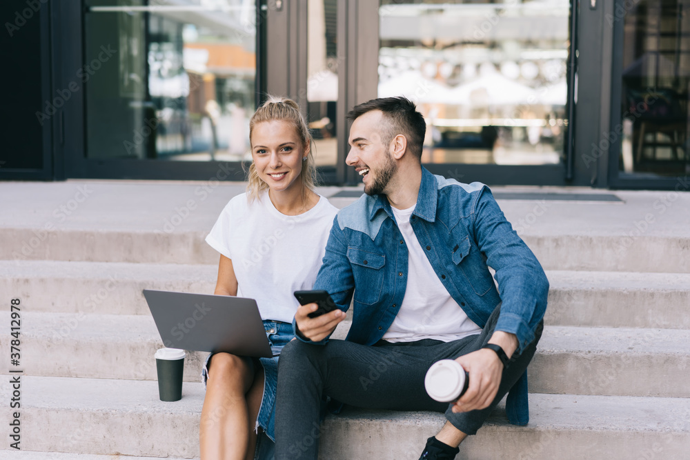 Cheerful couple with laptop and cellphone sitting on stairs - obrazy, fototapety, plakaty 