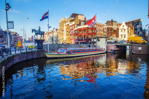 Monument to Queen Wilhelmina  on horse ,. pleasure(touristic) boat and water of canal and amazing medieaval architecture  of Amsterdam  Flag of the Netherlands