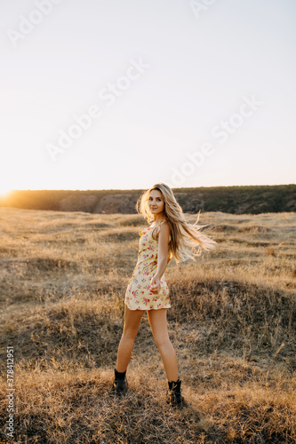 Young blonde woman smiling, standing in a field with dry grass in sunset light.