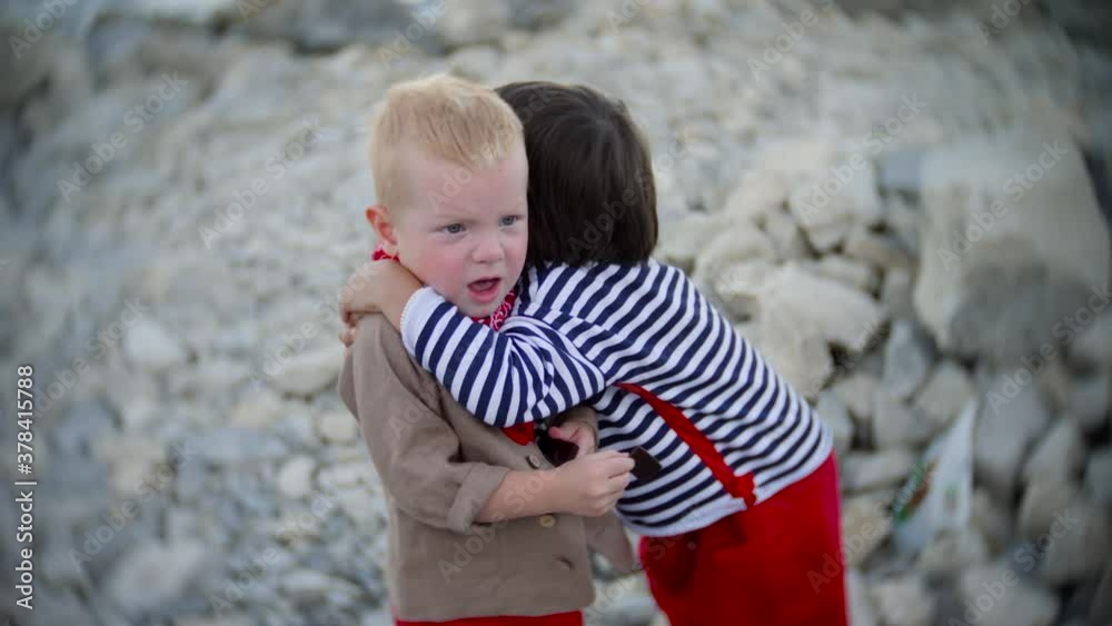 boy child hugs his friend on the beach with rocks in summer boy child hugs his friend on the beach with rocks in summer
