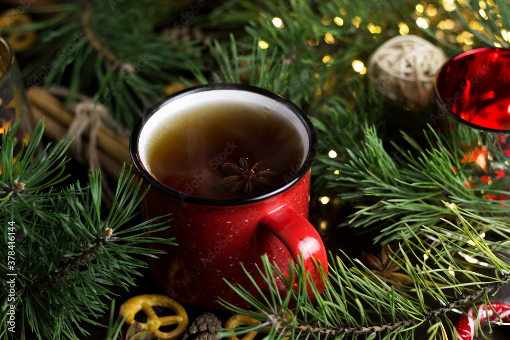 New year's tea party with spices. Red mug with tea surrounded by garlands, fir branches and spices New year's tea party with spices. Red mug with tea surrounded by garlands, fir branches and spices