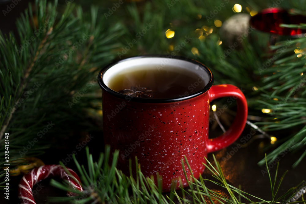 New year's tea party with spices. Red mug with tea surrounded by garlands, fir branches and spices