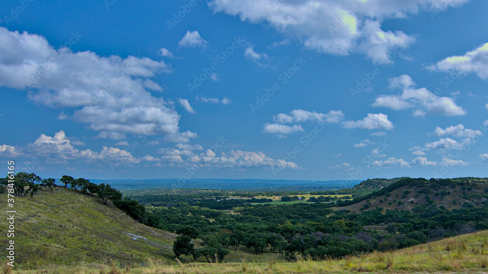 Rolling hills wine country central texas with lush green grasslands and forests with puffy white clouds in a blue sky on hot summer day.