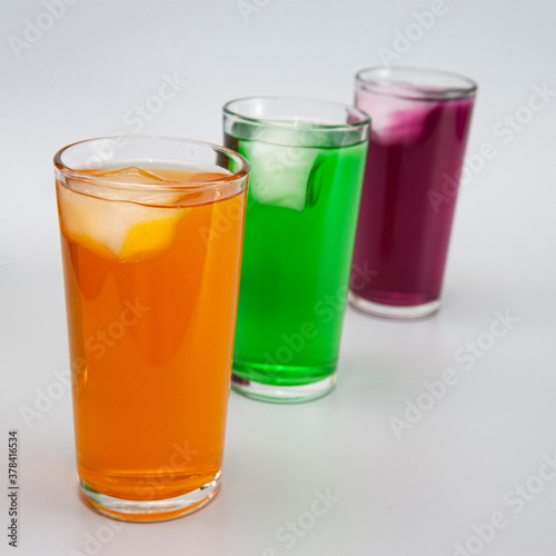 three glasses with different juices with ice on a white background 