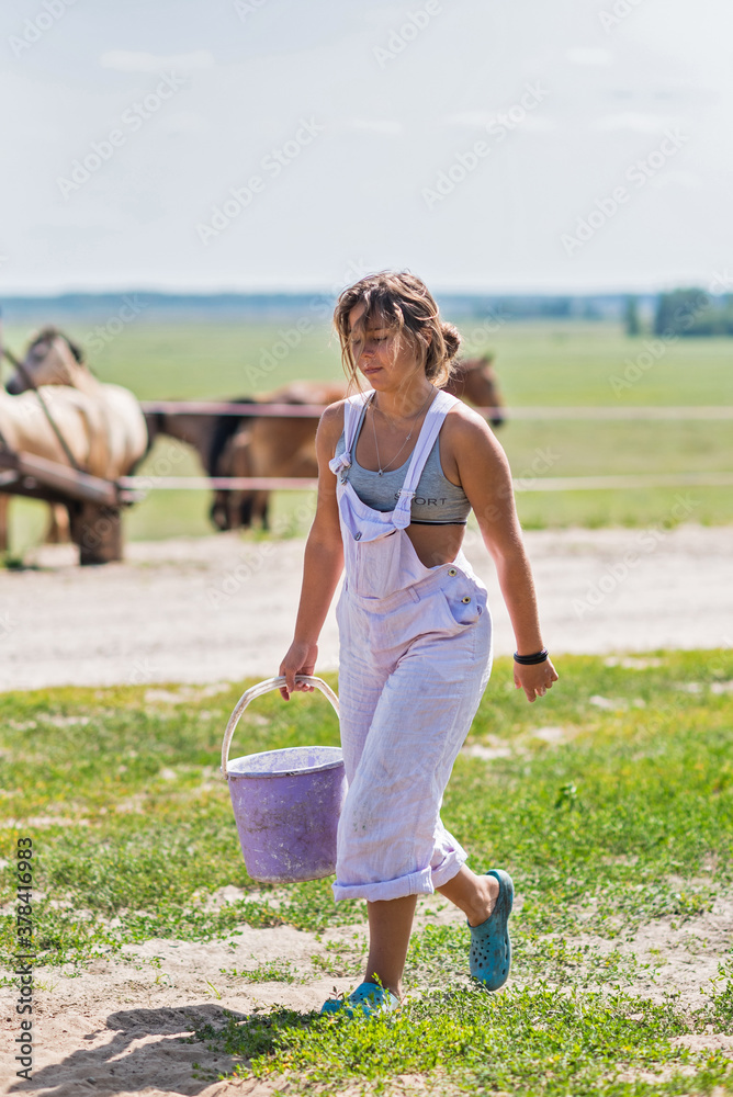 A girl farm worker walks across the field with a bucket.