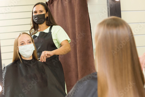 young woman in a mask gets her hair done in a beauty salon