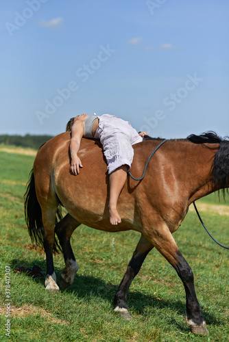 A young girl rides a horse lying down.