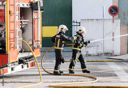 Cuadro en lienzo firefighters with a water hose pulling water to put out a fire