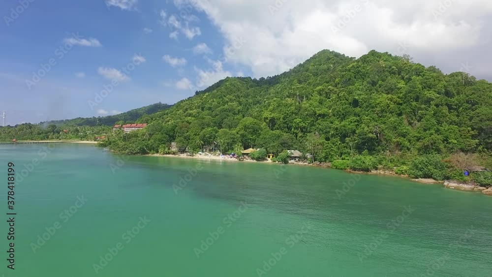 Aerial backwards dolly shot of small tropical beach on Koh Chang with small bungalows, jungle and turquoise sea