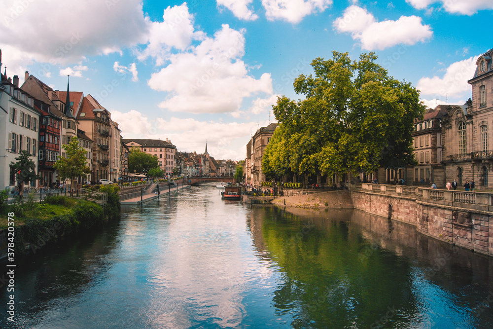 Scenic view of the Ill river in the historical city of Strasbourg, France on a bright summer day. Clouds and the beautiful riverfront reflect in the water.