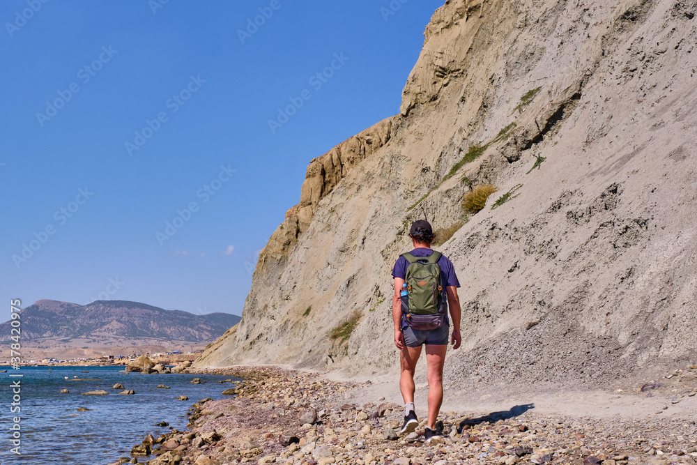 A tourist walks along the path of the rocky coast of Cape Meganom on the Black Sea, Crimea peninsula.