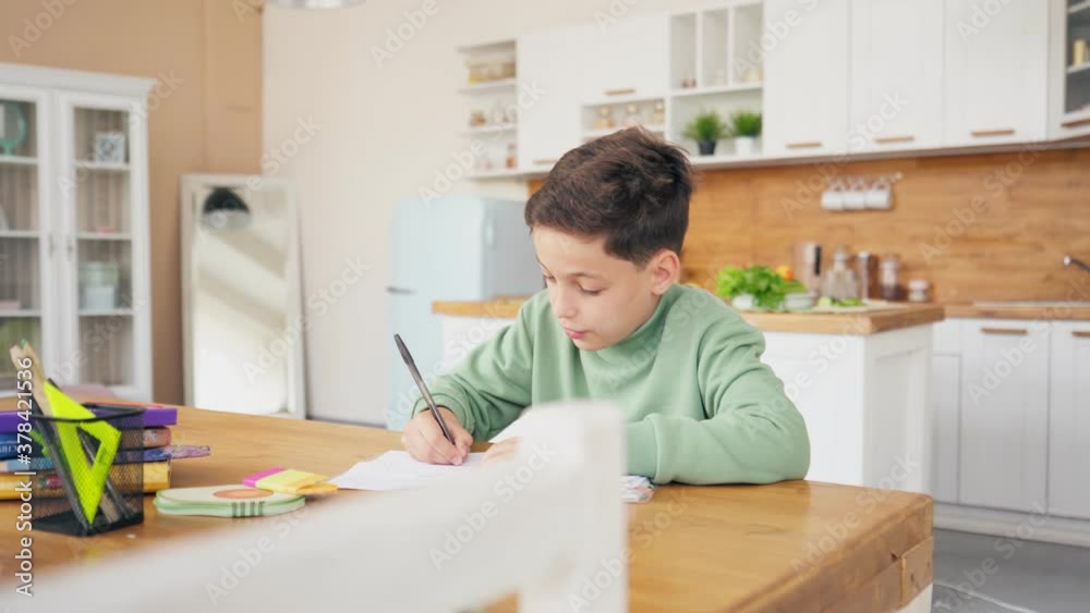 Boy In Kitchen Doing Homework And Chatting with laptop on the table Boy In Kitchen Doing Homework And Chatting with laptop on the table