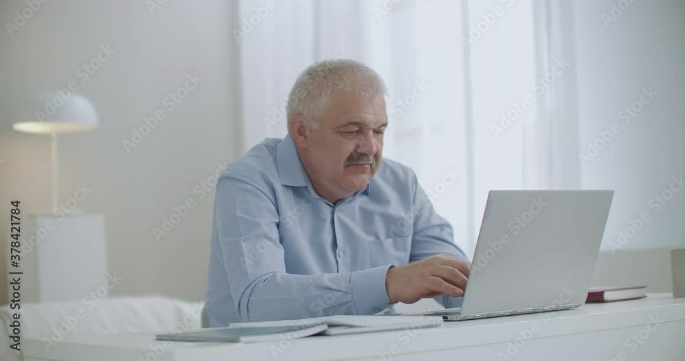 aged gray haired man is working remotely from home, communicating by chat, typing message on notebook with internet connection aged gray haired man is working remotely from home, communicating by chat, typing message on notebook with internet connection