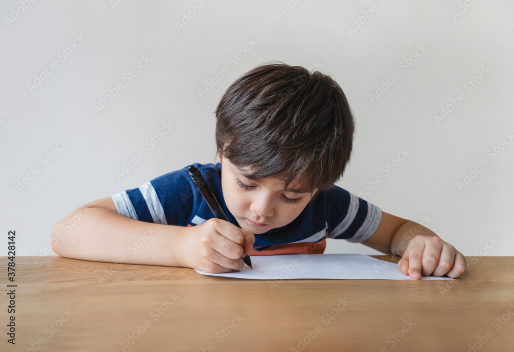 Portrait of school kid sitting alone doing homework, Child boy holding black pen drawing and writing on white paper on table, Elementary school and homeschooling concept Portrait of school kid sitting alone doing homework, Child boy holding black pen drawing and writing on white paper on table, Elementary school and homeschooling concept