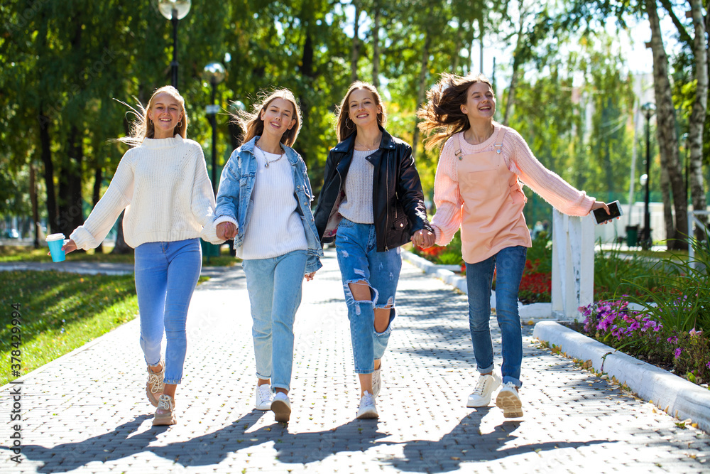 Four happy young girlfriends walking in autumn park