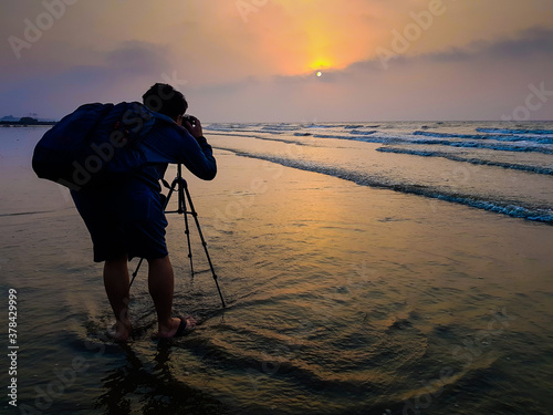 Photography A photographer with a bagpack taking photo of sunrise at the beach at dawn