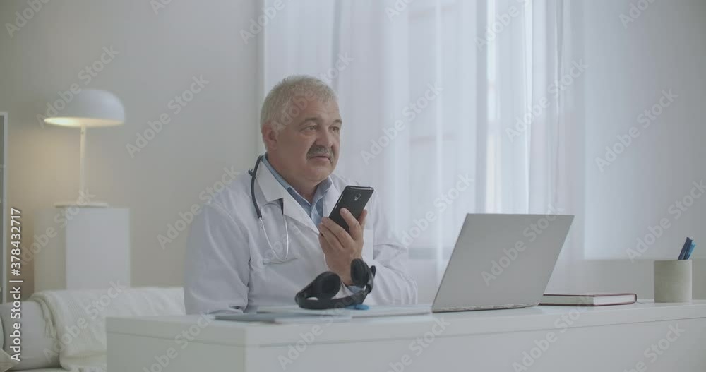 experienced therapist is consulting patient or chatting with colleague by cellphone, sitting in office of clinic, using speakerphone experienced therapist is consulting patient or chatting with colleague by cellphone, sitting in office of clinic, using speakerphone