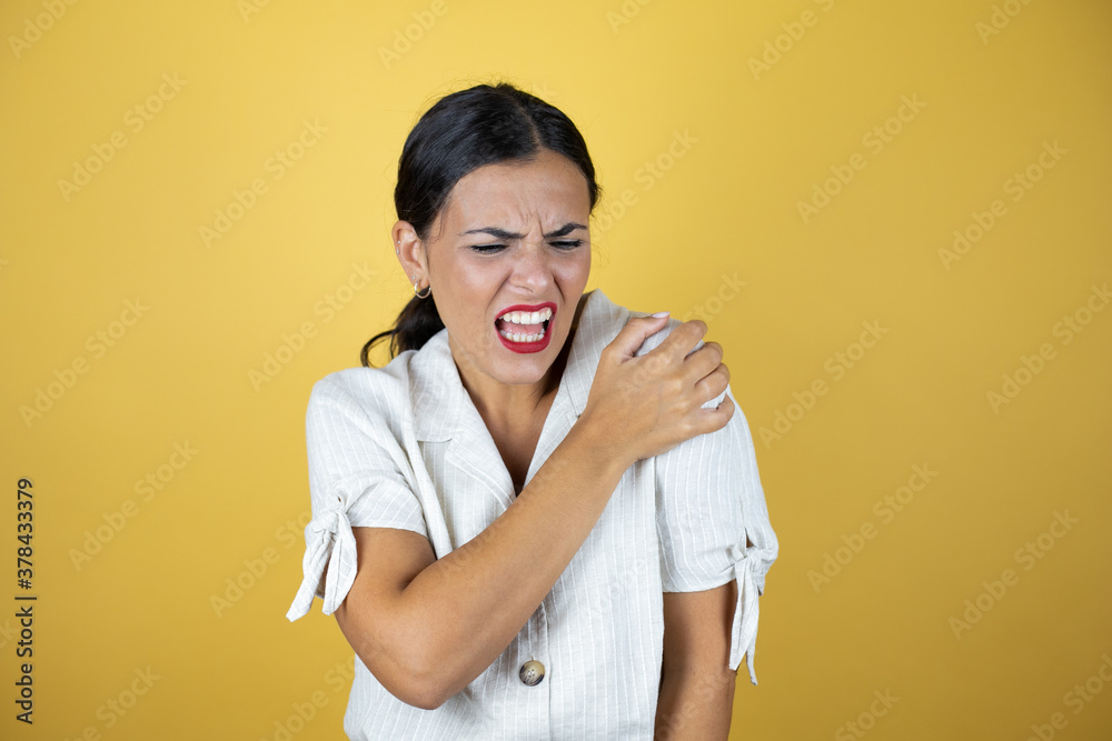 Beautiful woman over yellow background with pain on her shoulder and a painful expression. Beautiful woman over yellow background with pain on her shoulder and a painful expression.