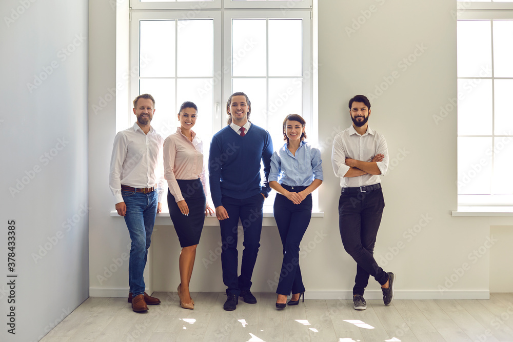 Group portrait of happy smiling company employees standing in modern office looking at camera