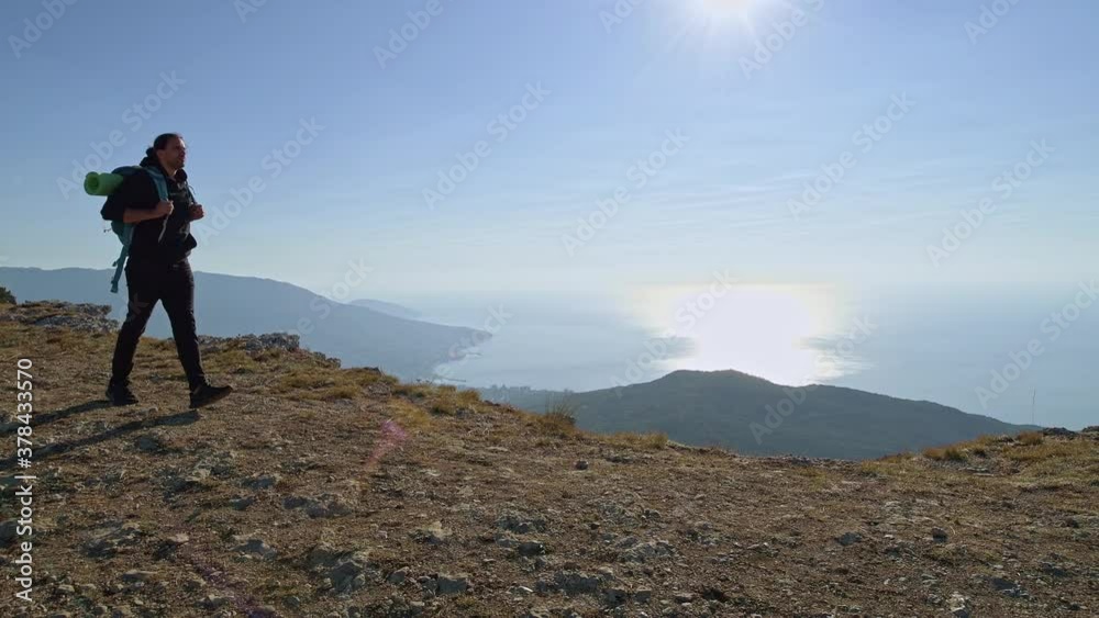 A young, male tourist climbs the mountains. A traveler with a backpack on his back stands on the top of the mountain A young, male tourist climbs the mountains. A traveler with a backpack on his back stands on the top of the mountain