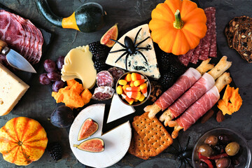 Halloween theme charcuterie platter. Top view table scene against a black stone background. Assorted cheese and meat appetizers.