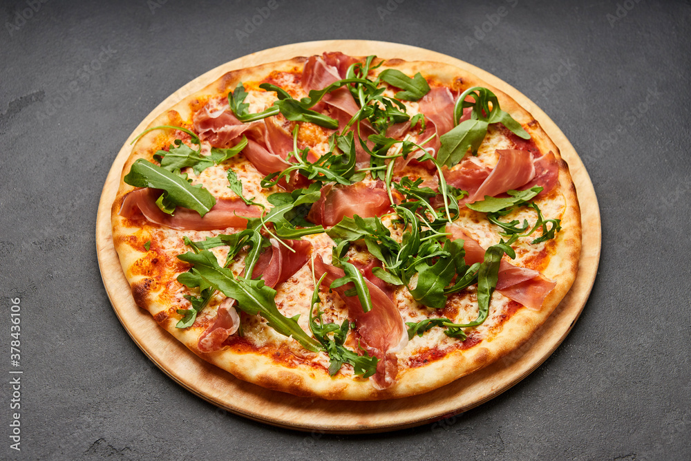 Delicious Italian Pizza with Parma ham and arugula, mozzarella cheese on dark background