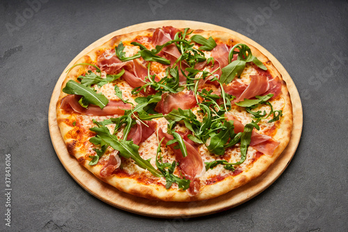 Delicious Italian Pizza with Parma ham and arugula, mozzarella cheese on dark background