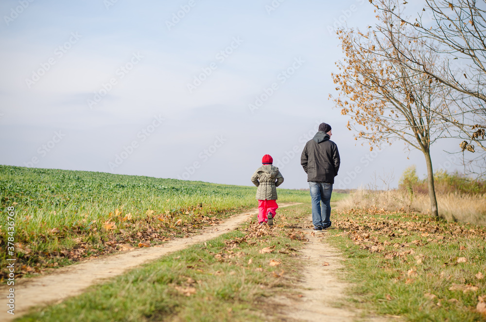 man and child walking together in autumnal colorful nature in rural path