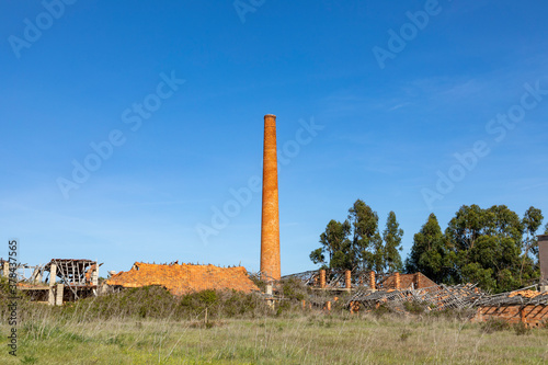 Fototapeta old rotten factory with damaged roof and old brick chimney in Sines, region Setu