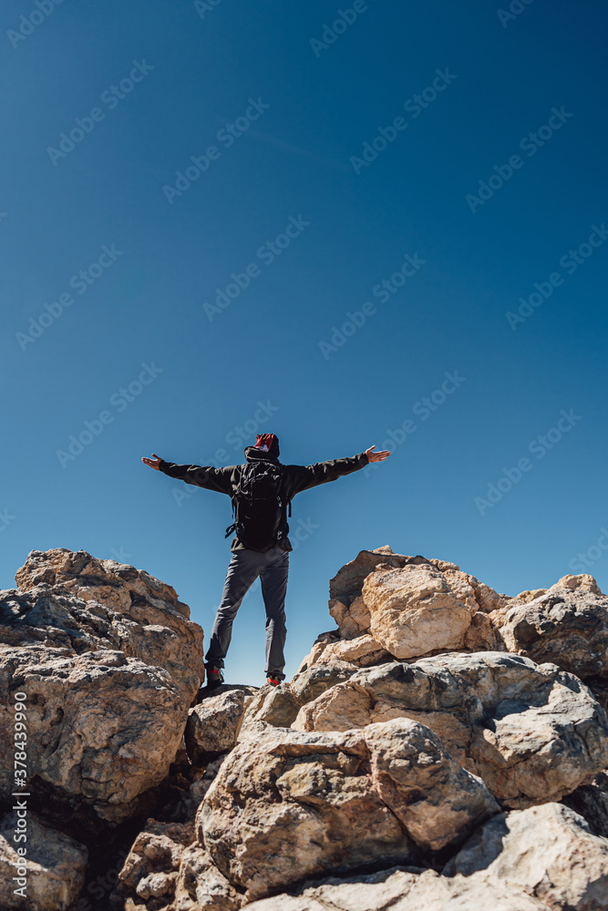 Hiker with backpack standing on top of a mountain with raised hands. Success, freedom and happiness, achievement in mountains peak. Active sport concept.