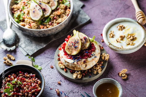 tasty healthy dish with figs fruits, nuts, honey, camembert cheese, couscous and pomegranate seeds and figs