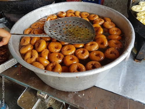 fried food vada dipped in sweet syrup in a big aluminium container photo