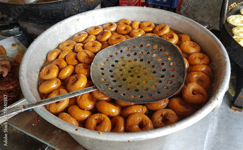 fried food vada dipped in sweet syrup in a big aluminium container photo