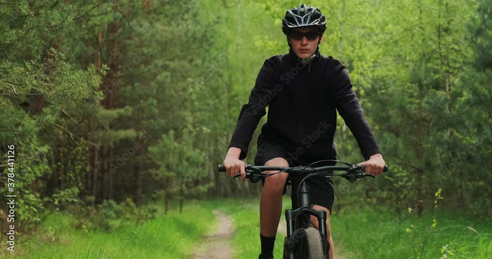 Young  man cyclist rides on a forest road. Teenager on a mountain bike rides through the forest. Man in a Bicycle helmet rides an mtb bike.