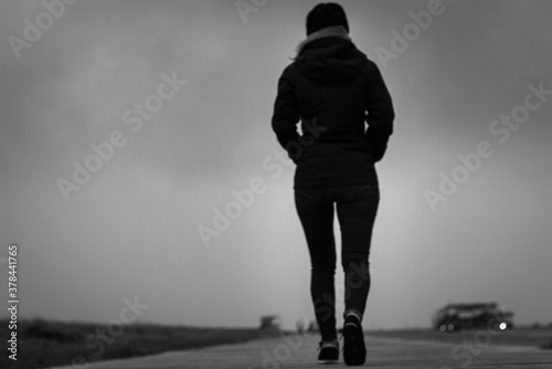 Unrecognizable woman walking away on a wooden footpath at north sea beach in black and white.