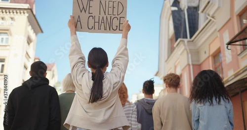 Asian woman in back of protest demonstration holding a poster We need a change. Student activist.