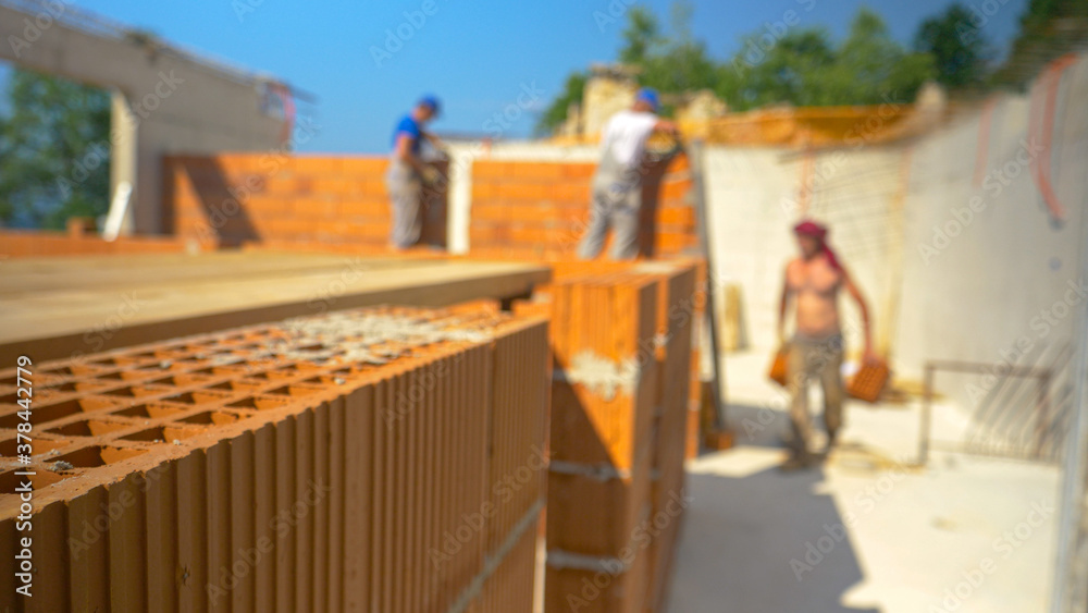 CLOSE UP, DOF: Blurry shot of contractors laying bricks and building walls.