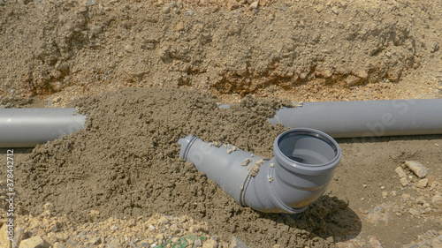 CLOSE UP: Fresh concrete covering plastic sewage tubing dries in the summer sun.