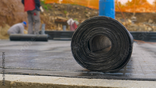 MACRO: Roll of tar lies on the ground as contractors work in the background.