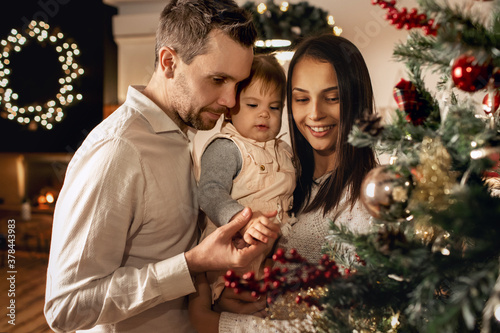 young family greets the new year and christmas, dad and mom hold their daughter in their arms and decorate the Christmas tree