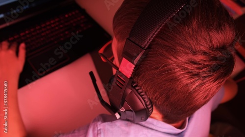 A boy in headphones playing online computer game at night, he is immersed in atmosphere of virtual reality
