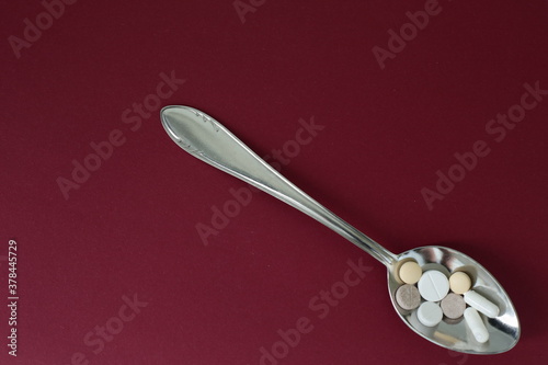 Spoon with pills and pills on burgundy background
