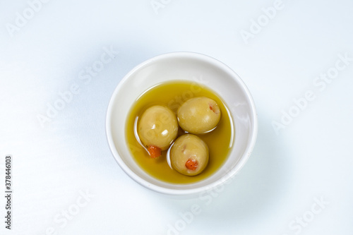 Green olives in a small casserole with olive oil on a white surface background
