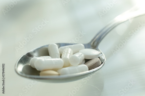 Tablets and pills lie in a metal spoon on a glass table