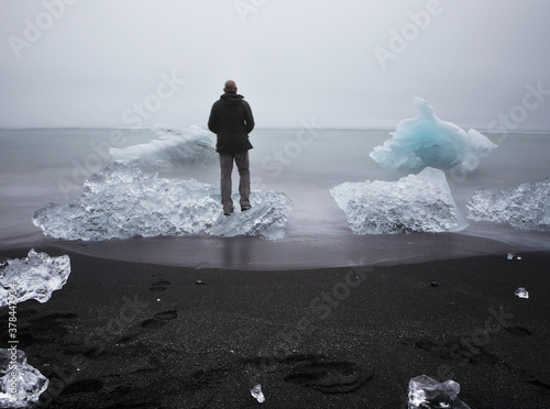 Vászonkép A tourist stands on an iceberg washed ashore at Diamond beach.