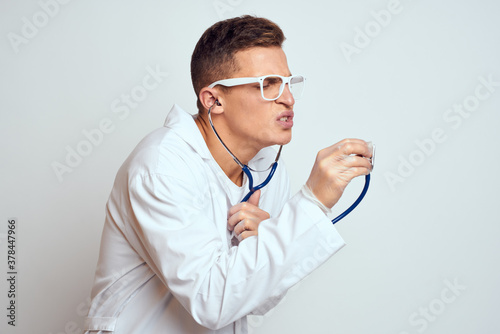 doctor in a medical gown with a stethoscope and glasses on a light background cropped view portrait