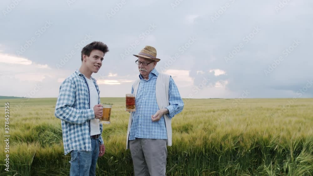Two happy farmers hold mugs with light and dark beer and talk in barley field Two happy farmers hold mugs with light and dark beer and talk in barley field