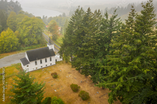 Aerial View of a Little White Church on a Foggy Morning. Atmospheric look at  a Congregational Church and the graveyard accompanying the building. The Salish Sea can be seen in the background.